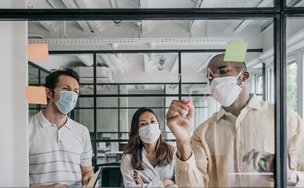 team wearing masks around a whiteboard