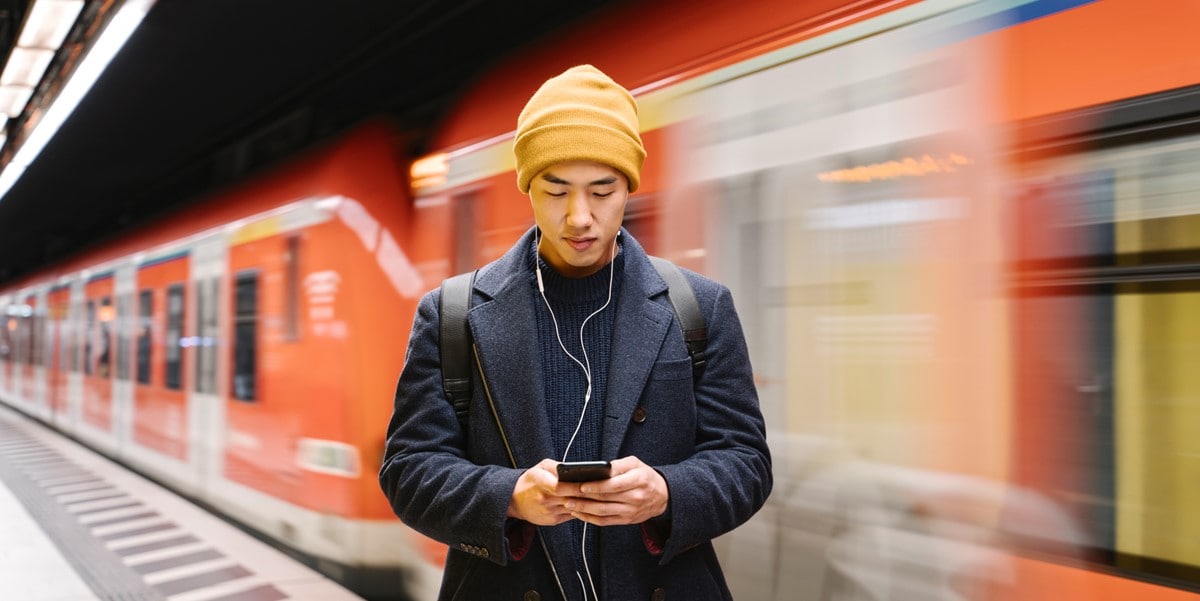 man looking down at phone standing in front of moving train
