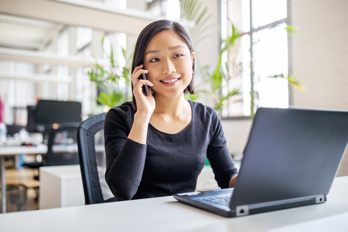 Lady sitting at desk on mobile with laptop open