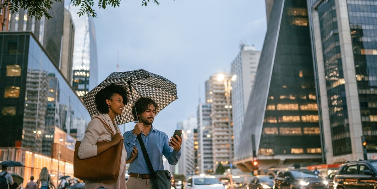 two travelers in city under umbrella, waiting for a ride